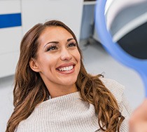 Woman smiling at reflection in handheld mirror