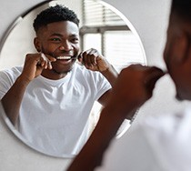 Patient smiling while flossing his teeth in bathroom