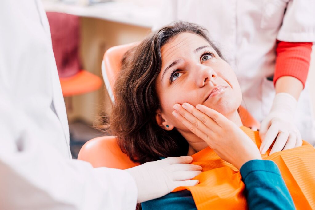 Woman in dental chair holding hand to jaw in pain with dentist touching her shoulder